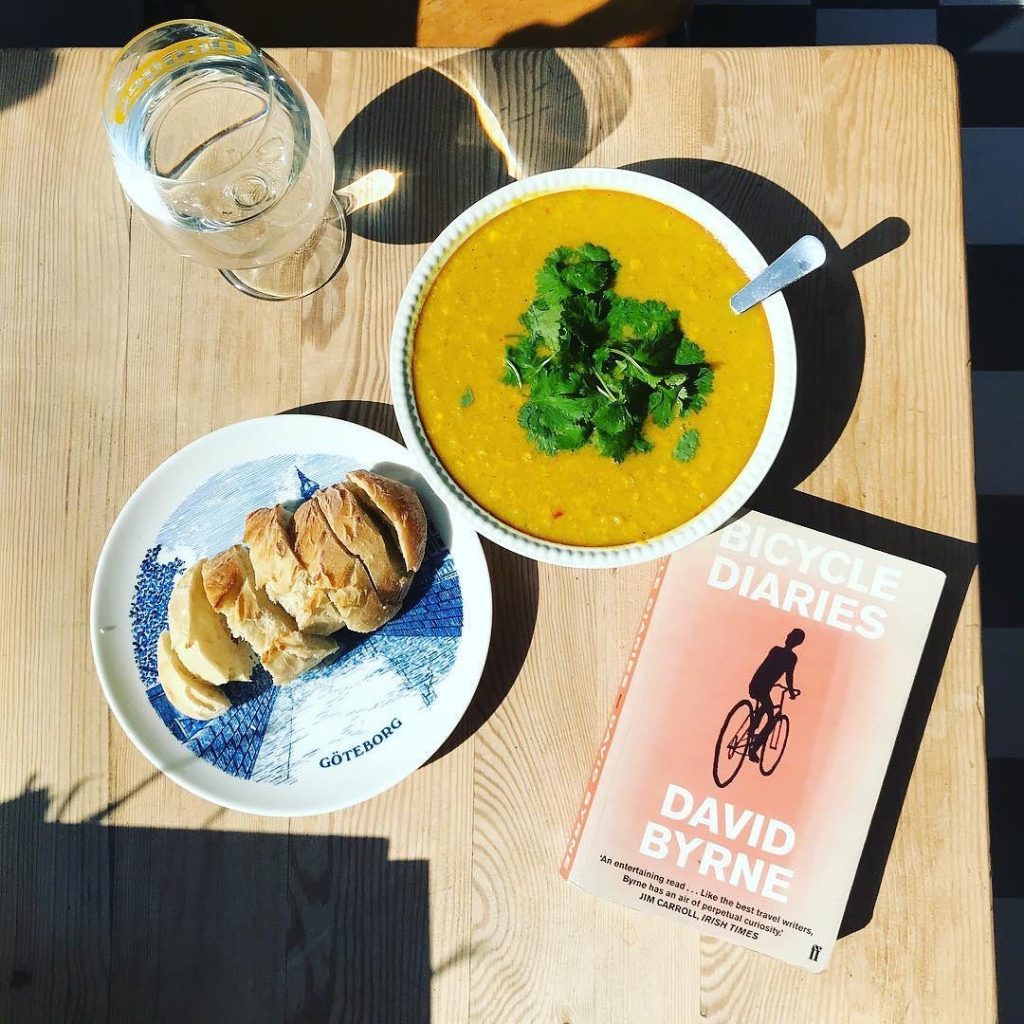 En tallrik majssoppa med en tallrik med nybakat bröd ligger på ett bord bredvid boken Bicycle Diaries av David Byrne.